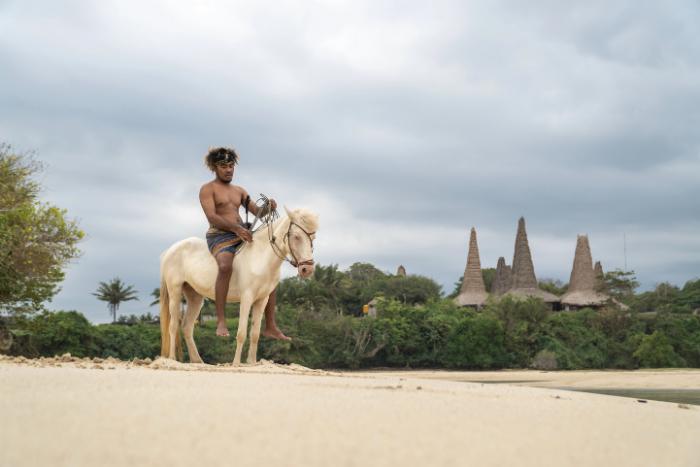 Horse riding on the beach with Ratenggaro traditional village in the background in West Sumba.