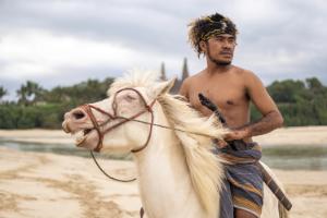 Local Sumba man riding a horse along the beach in traditional clothing.