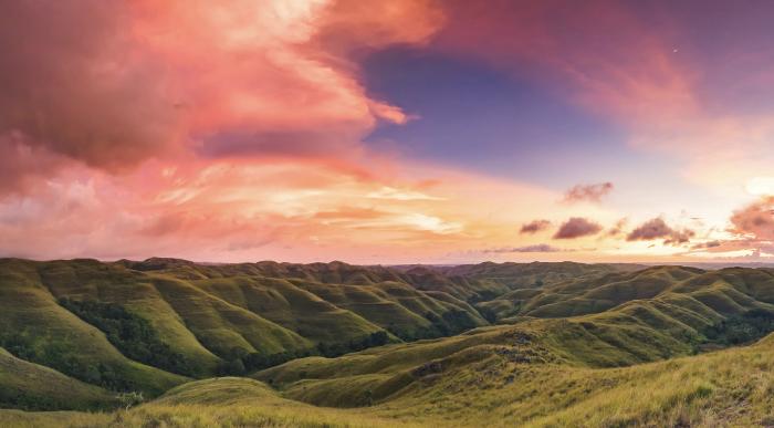 Rolling green hills of East Sumba at sunset with colorful sky.