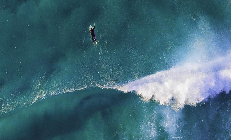 Aerial view of a surfer paddling in turquoise water near a breaking wave in Sumba.