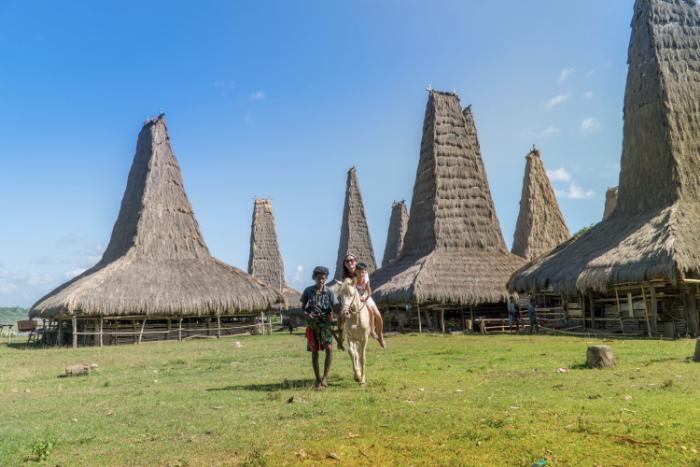 Ratenggaro Village in Sumba with traditional tall thatched houses and horse riding visitor.