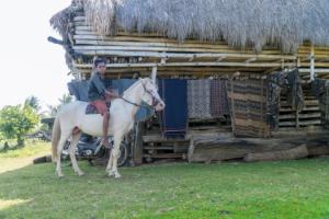 Local Sumba man riding a horse in front of a traditional Sumba house in a rural village.